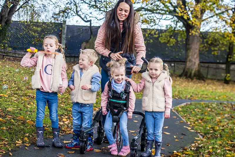 A girl using a Leckey gait trainer with her family in a park